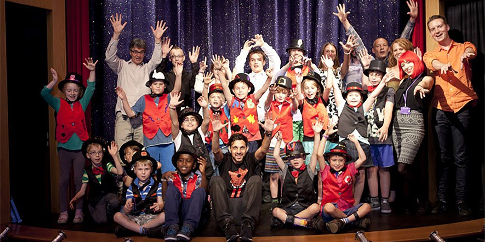 A large group of children with magicians, including Dynamo, on stage