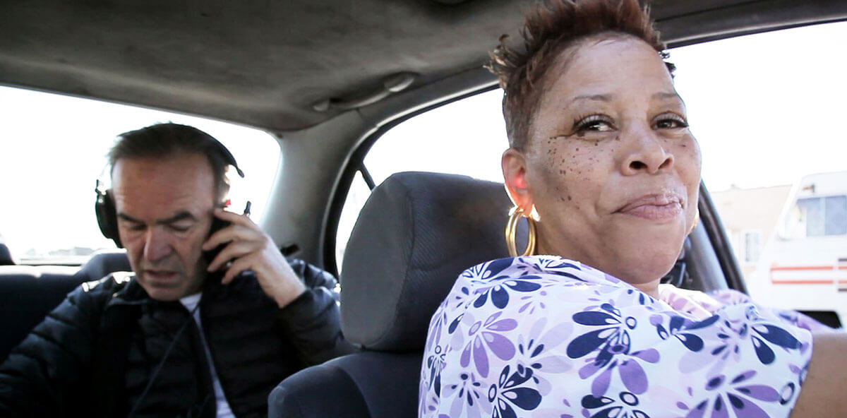 Tales of the Grim Sleeper: Director Nick Broomfield (left) with headphones and contributor Pam in foreground driving a car